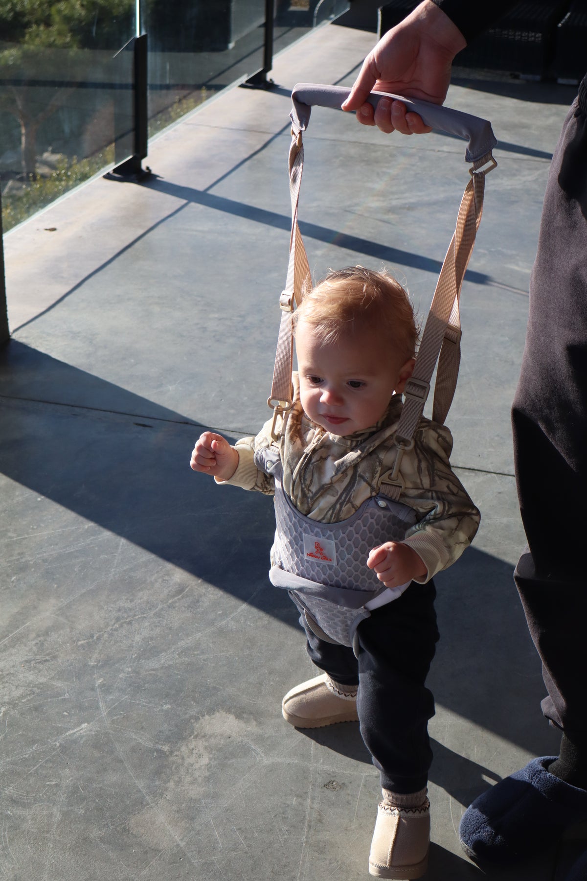 Toddler standing confidently in the Rest and Nurture baby walking harness on a sunny patio