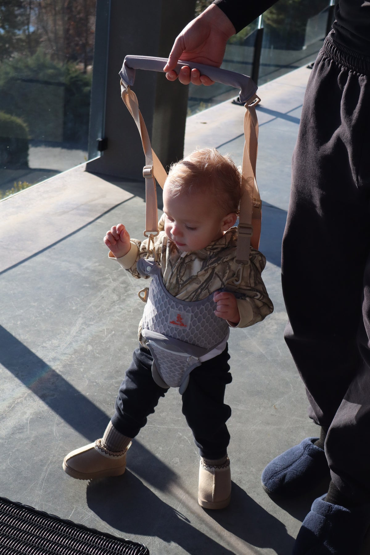 Baby practicing balance in the walking harness with gentle upright support from a parent