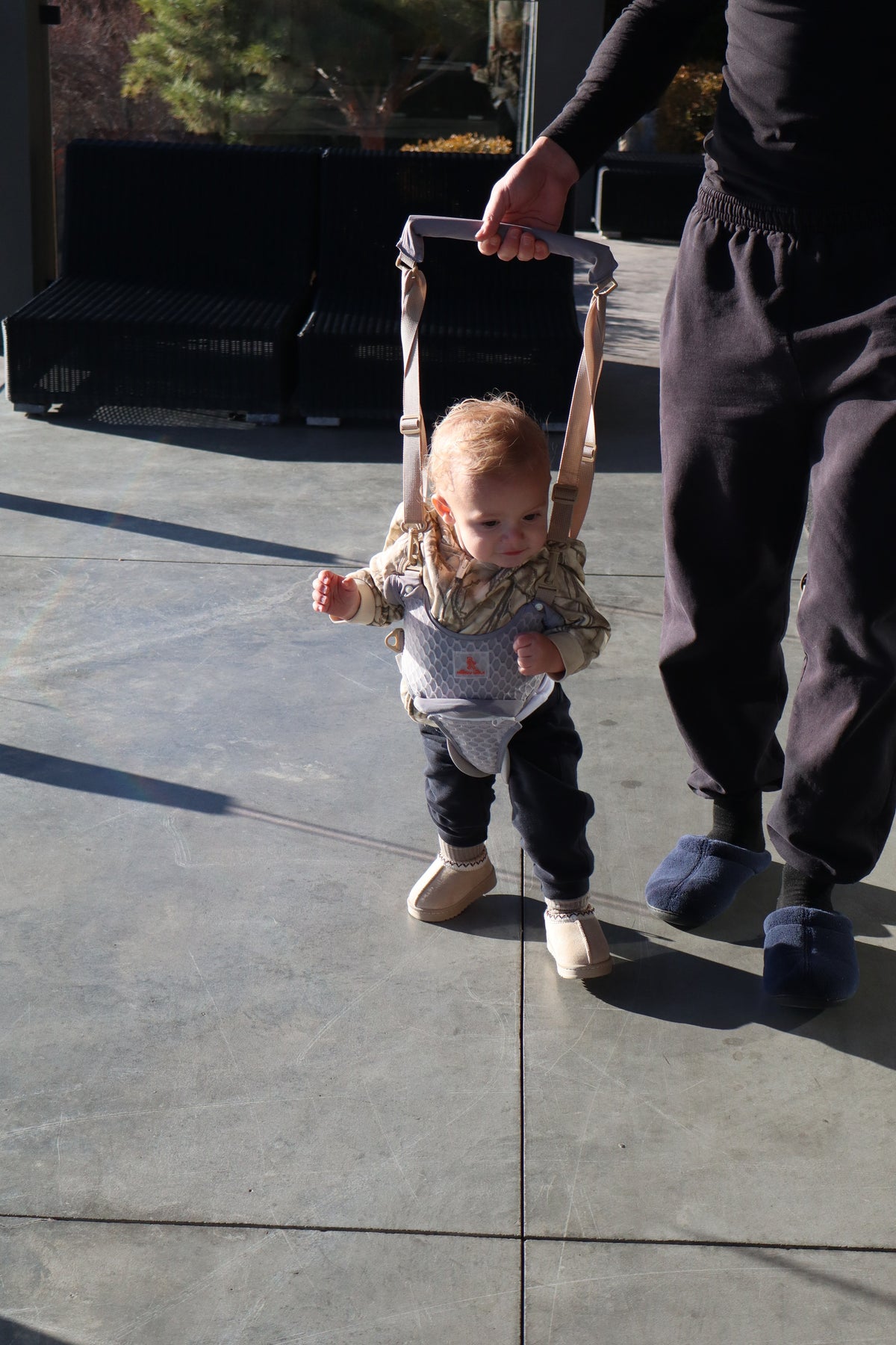 Parent walking beside a toddler learning to walk in the baby walking harness